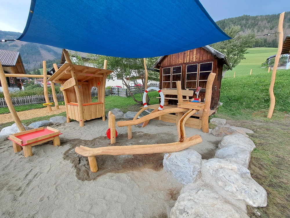 Naturspielplatz mit Holzboot und Spielhaus unter einem Sonnensegel